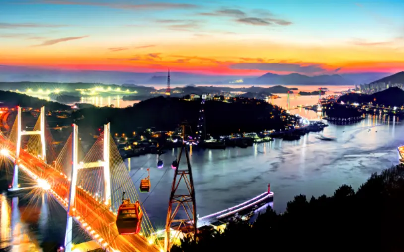 노을이 지는 저녁 밝게 켜진 다리조명 위로 운행중인 해상케이블카