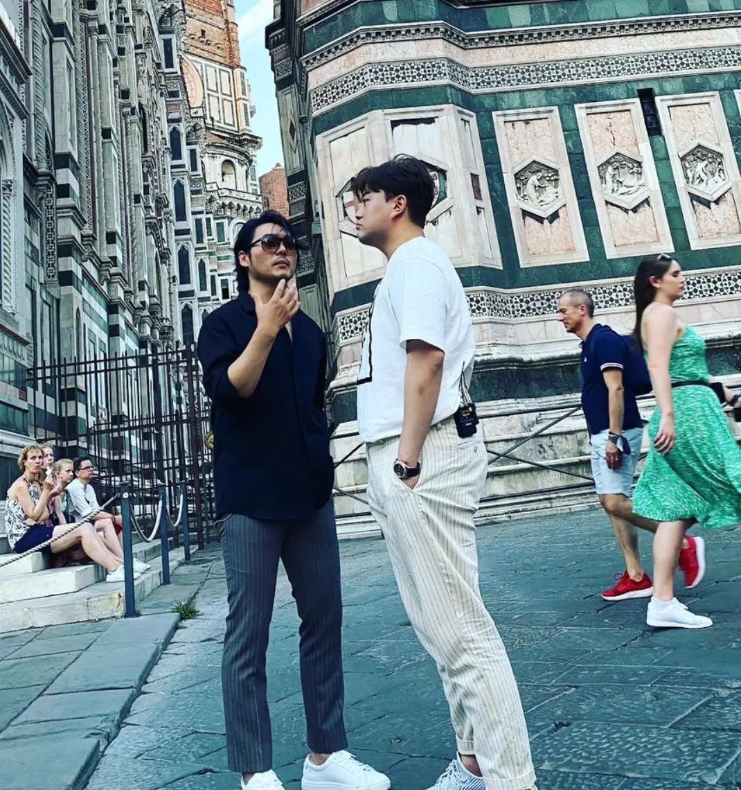 유럽의 고풍스러운 도시 좌측 검은 옷을 입은 남자와 흰옷을 입은 김호중이 서있는 옆모습