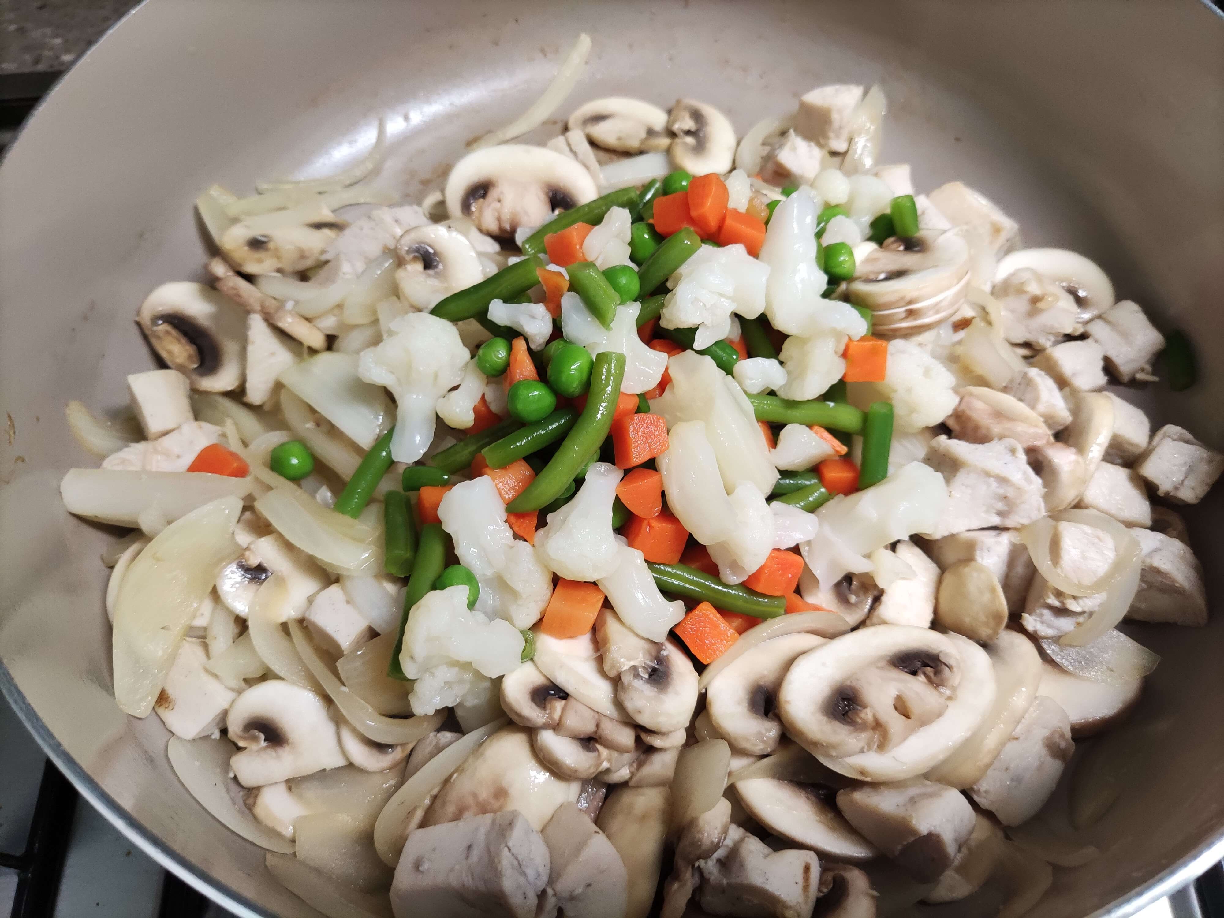 던 닭가슴살, 양파, 양송이버섯 위에 냉동 채소 믹스 (콜리플라워, 그린빈, 당근, 완두콩)를 넣는 모습