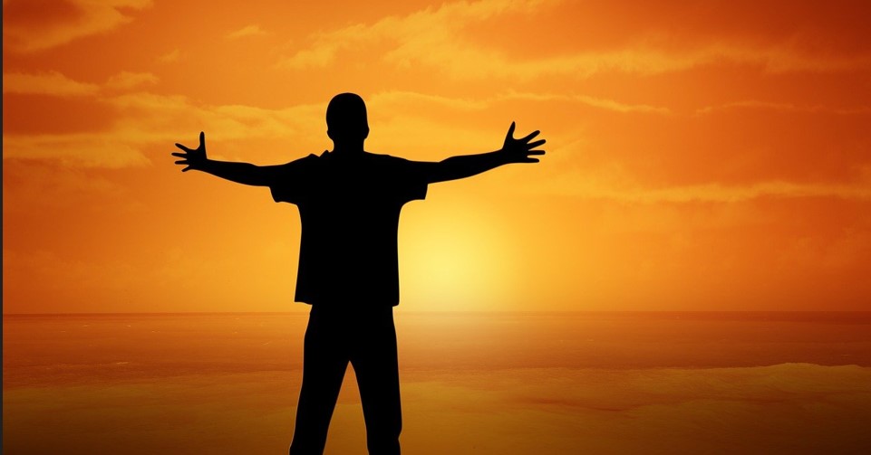 한 소년이 양팔을 벌리고 일몰을 바라보고 서있는 뒷모습을 찍은 사진