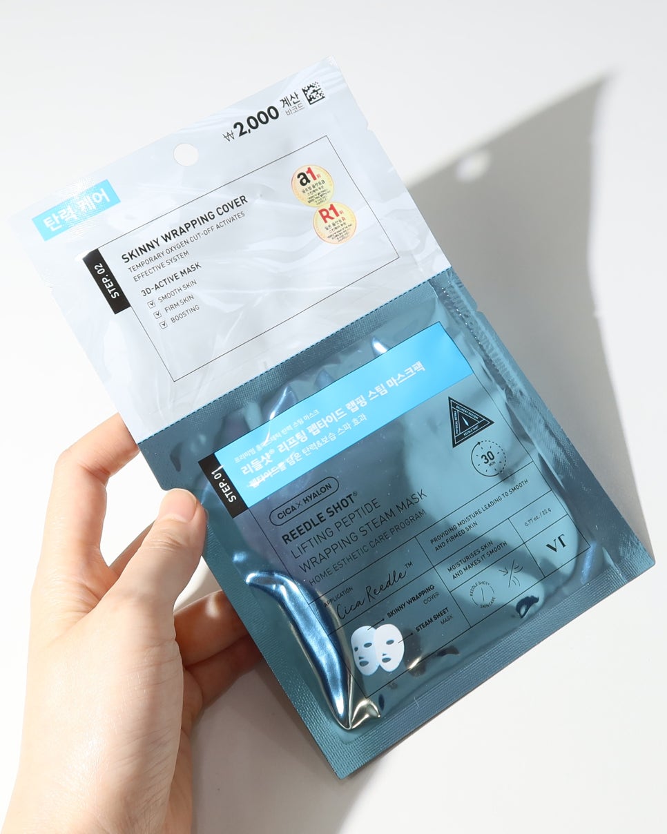손으로 'VT 리들샷 리프팅 펩타이드 래핑 스팀 마스크'를 들고 있는 모습, 패키지 전면이 강조됨.