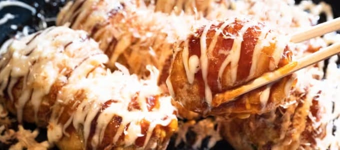 흰색 소스와 갈색 소스가 올라간 동그란 타코야기를 젓가락으로 집고 있다