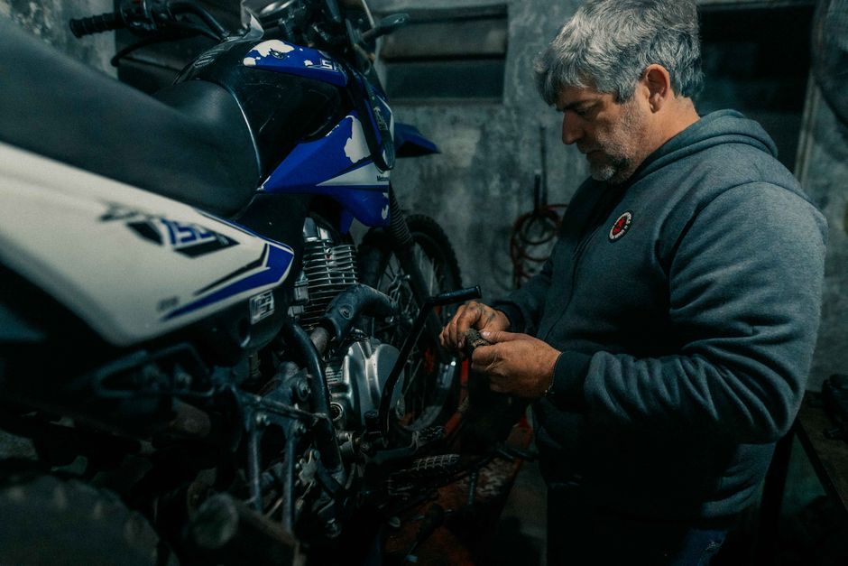 An adult man repairs a motorcycle in a dimly lit garage, showcasing mechanical expertise.