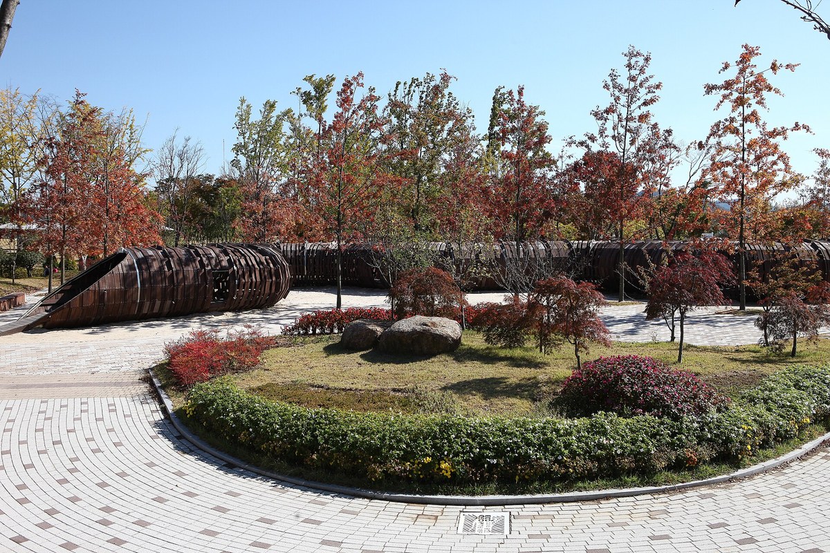 Red autumn trees around a paved plaza with a curved wooden structure at Suncheon Bay National Garden