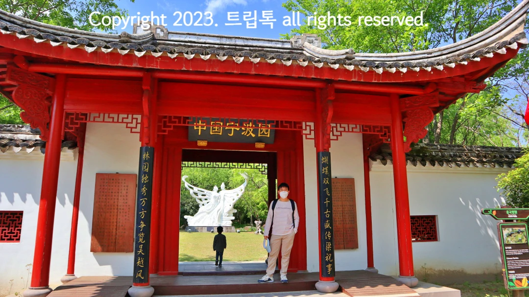 붉은 나무기둥으로 이루어진 대문과 기와 모양의 입구에 한자가 써있다. 안쪽으로 하얀 나비조각상이 보인다.