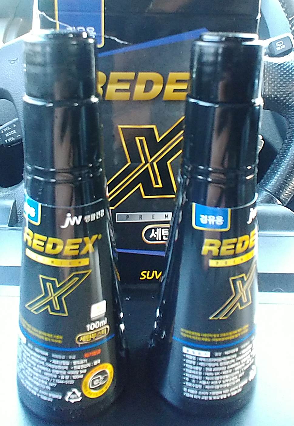 아래가-넓고-위가-좁은-원통형-검은색-플라스틱통-두개가-있고-뒤에-검은색-박스와-자동차-핸들이-있다