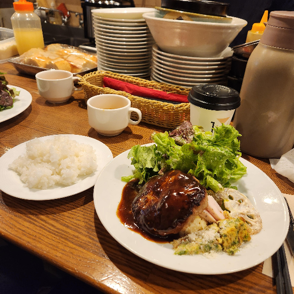 소스가 올라간 함박스테이크와 야채들이 접시에 담겨 있다. 다른 접시에는 밥이 그리고 커피 잔이 테이블에 같이 올려져있다.