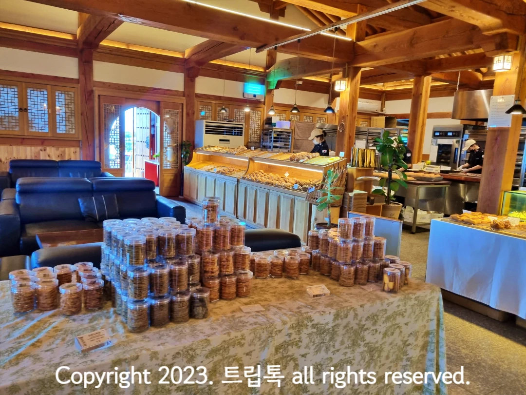한옥으로 되어서 나무도 벽과 기둥이 이루어져있고 앞에 테이블에 과자가 쌓여있고 그 뒤에 직원이 빵을 정리한다