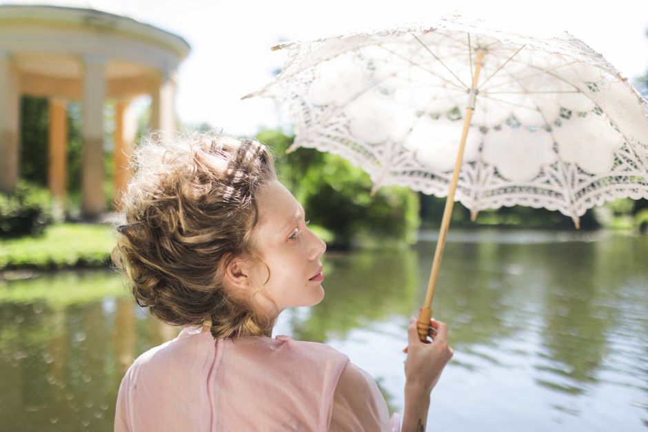 Caucasian woman with umbrella by the lake in summer, evoking elegance and tranquility.