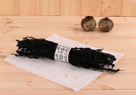 나무 바닥에 커다란 마른 미역 한 뭉치가 놓여있고, 뒤에는 작은 도자기 단지 2개가 있다.