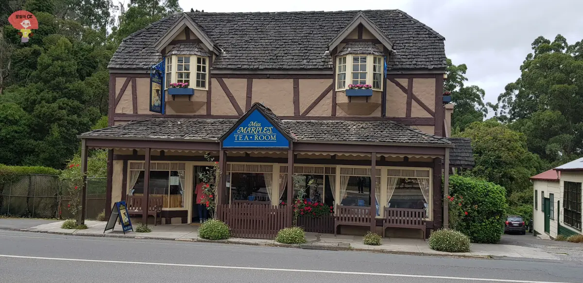 호주-멜버른-단데농-사사프라스-미스-마플스-티룸-외관 영국식 전통 목조 건물에 화분과 꽃이 장식되어 있으며, 파란색 간판이 건물 중앙에 걸려 있다."