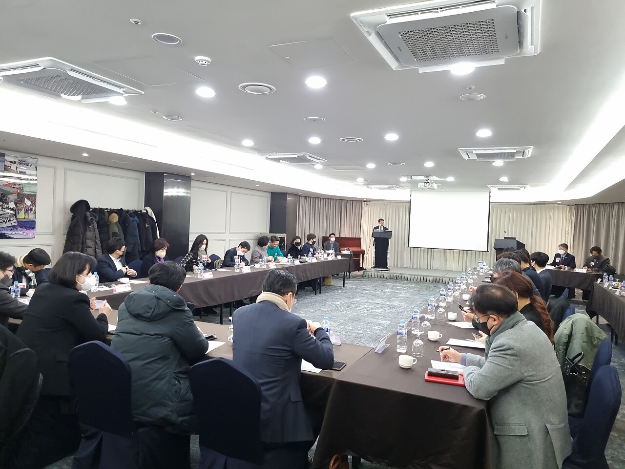 비엔아이 그랜드챕터 주간회의의 전경입니다. ㄷ자 테이블에 40명의 사람이 둘러싸여 단상의 ppt 자료를 보면서 회의하는 모습입니다. 기버스게인 비엔아이 그랜드챕터