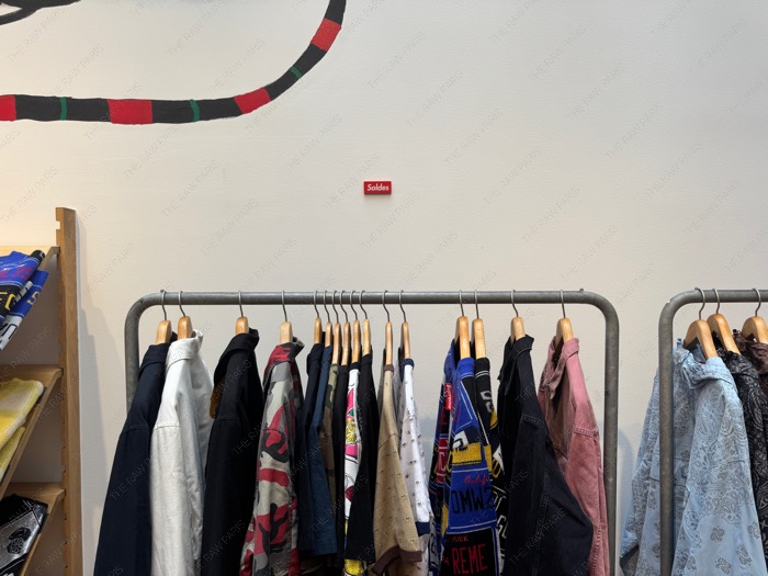 A minimalist red Soldes sign on a white wall above a clothing rack inside the Supreme store in Paris