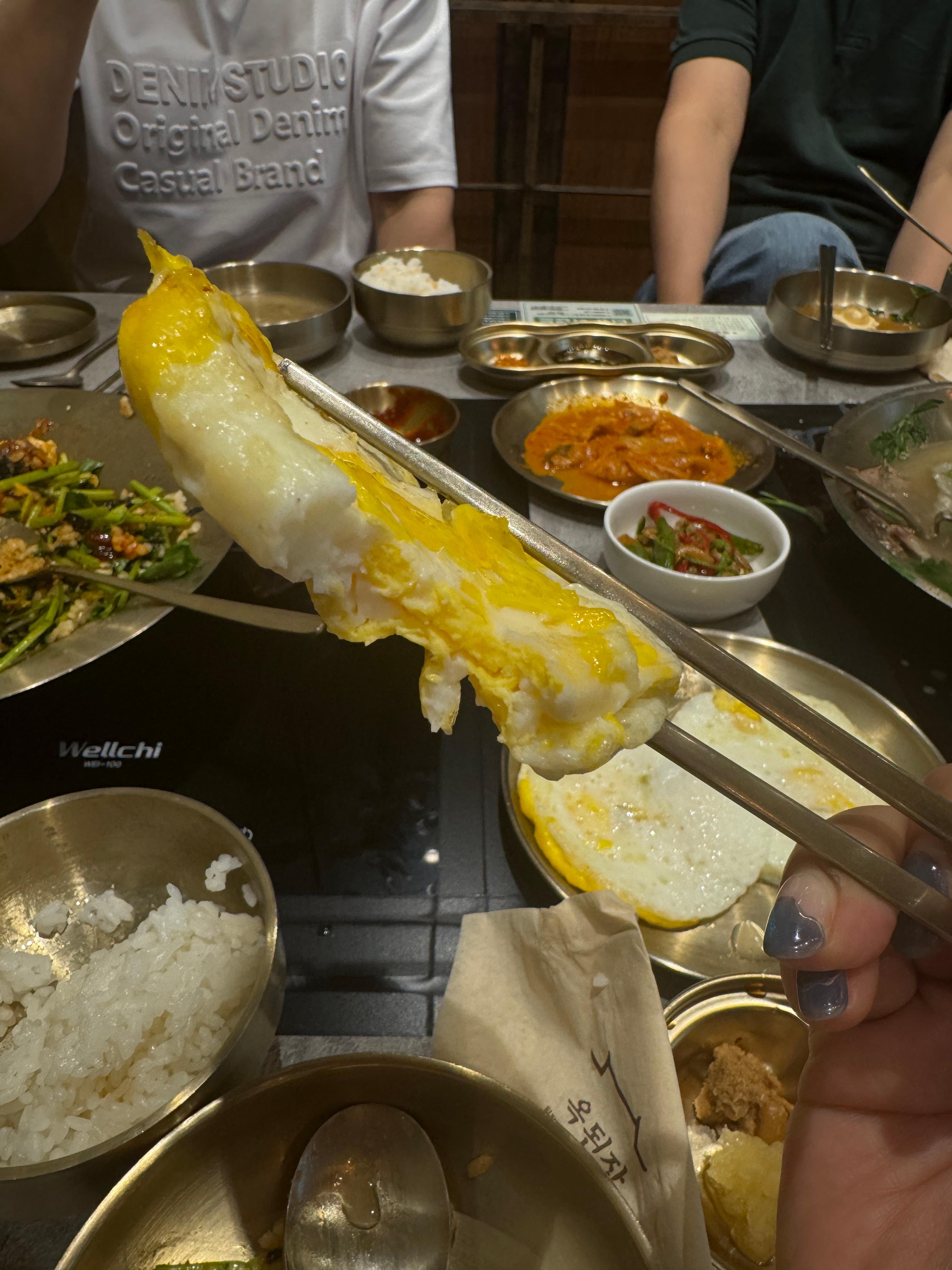 젓가락으로 집은 노른자 반숙 계란후라이&amp;#44; 뒤로는 김치찜과 밥이 보이는 미금역 옥된장 밑반찬