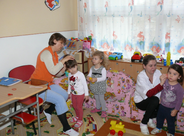 교사들이 유아를 돌보고 있는 실내 아동복지 공간. 장난감과 유아용 가구가 갖춰진 환경에서 아이들이 일상적인 돌봄을 받고 있는 모습.