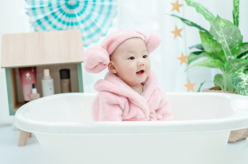 신생아 목욕 방법 안내, 분홍 수건을 쓴 아기 욕조 목욕 모습, 신생아 목욕 물 온도와 마사지 방법 설명 이미지