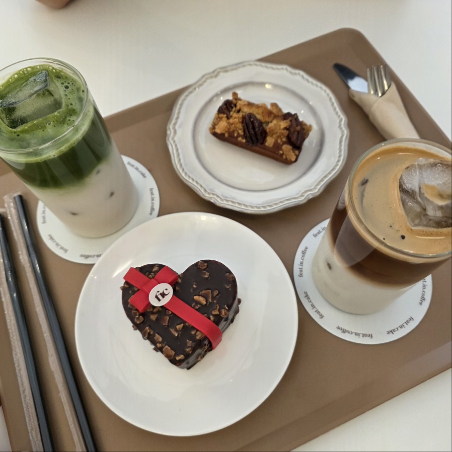 말차 라떼와 아이스 라떼, 하트 초콜릿 케이크와 휘낭시에가 놓인 카페 디저트 트레이