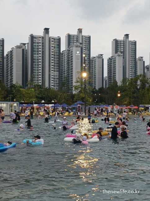 가로등 불빛 아래 수많은 가족과 시민들이 야간 물놀이를 즐기고 있는 잠실 물놀이장 풍경