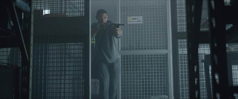 Rebel Ridge 영화 장면, 주인공이 어두운 창고에서 총을 겨누는 모습