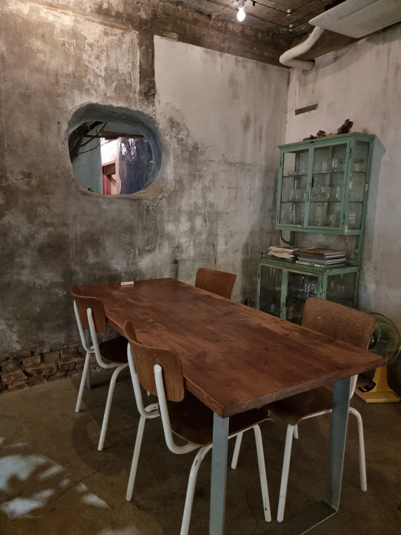 그린색-철제-찬장-콘크리트-벽면-동그란-창-그아래-나무테이블