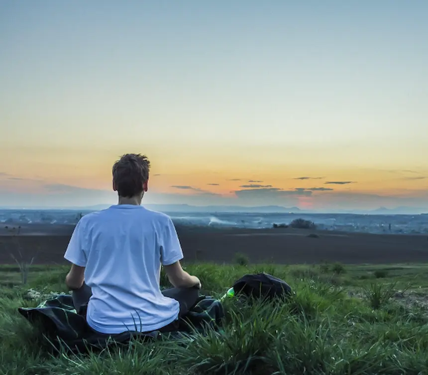아침 일출을 보며 들판에 앉아 명상하는 남자의 뒷모습