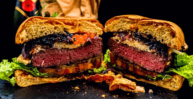 두툼한 소고기와 검정 캐비아가 가득 들어있는 커다란 햄버거를 반으로 자른 단면이다.