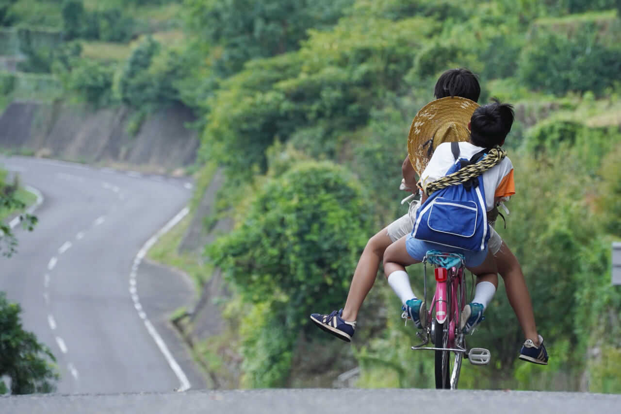 히사와 타케가 함께 자전거를 타고 내리막길을 내려가는 뒷모습을 담은 장면