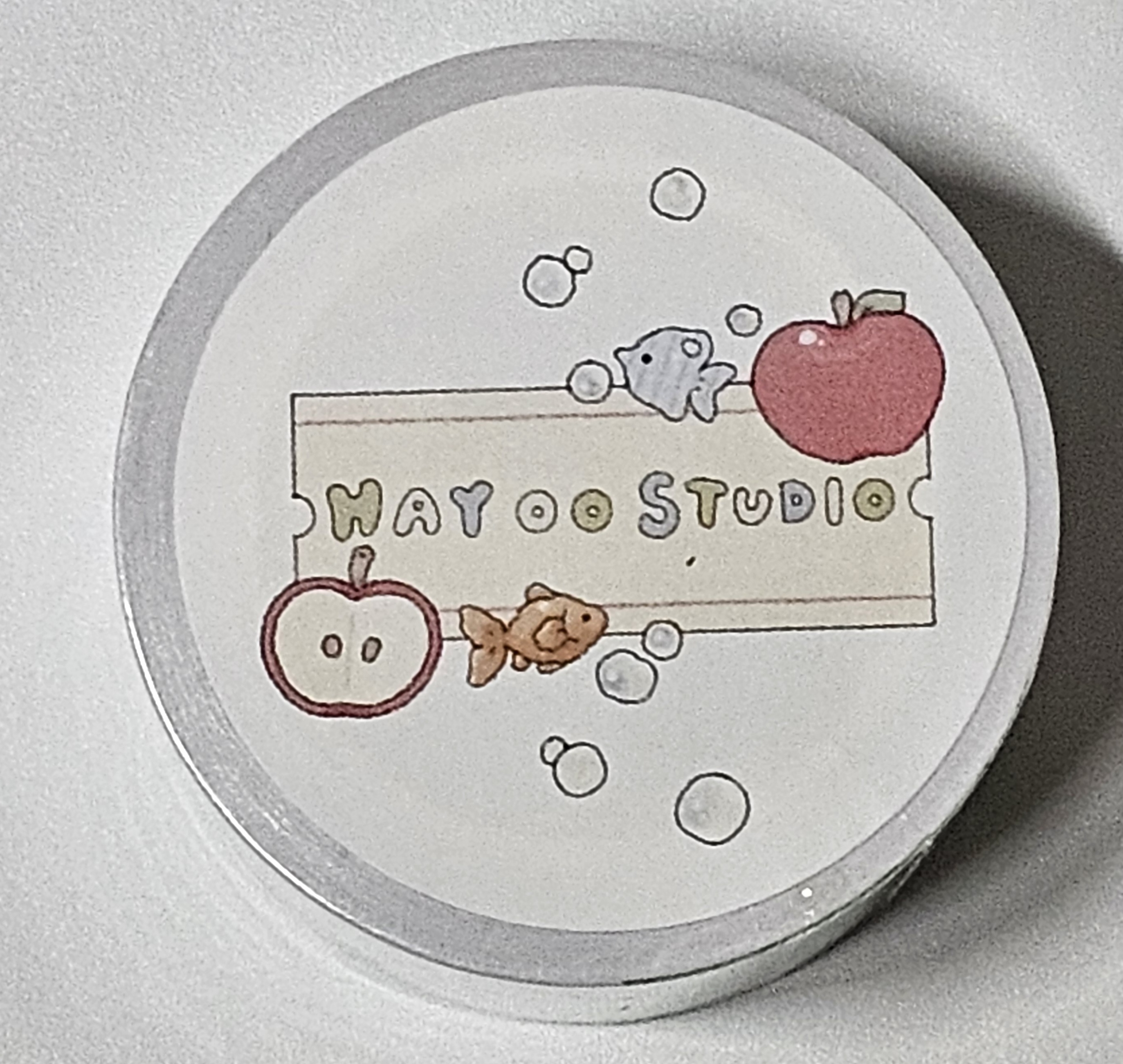흰 배경 위에 ‘HAY OO STUDIO’ 로고가 적힌 원형 라벨. 사과와 금붕어, 파란 물고기, 작은 물방울 그림이 함께 그려져 있는 귀여운 디자인.