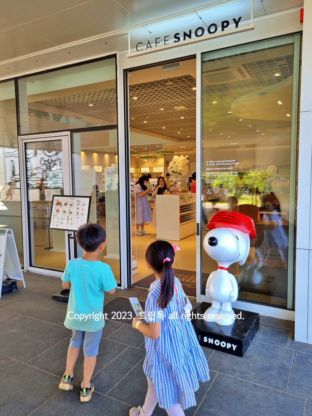 카페스누피로 통유리로 된 입구에 아이 2명이 있다.