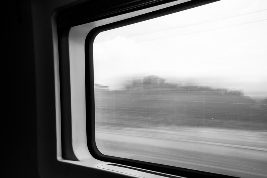 Blurred landscape seen through a train window, capturing motion and speed in black and white.