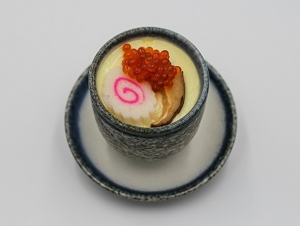 부드러운 계란찜이 받침이 있는 동그란 회색 도자기 그릇에 담겨있다. 계란찜 위에는 연어 알, 표고버섯 등이 장식으로 올려있어서 더 먹음직스럽게 보인다.