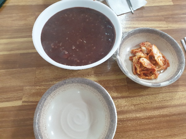 밥알이 보이는 팥죽 그리고 김치가 함께 테이블 위에 놓여있다.