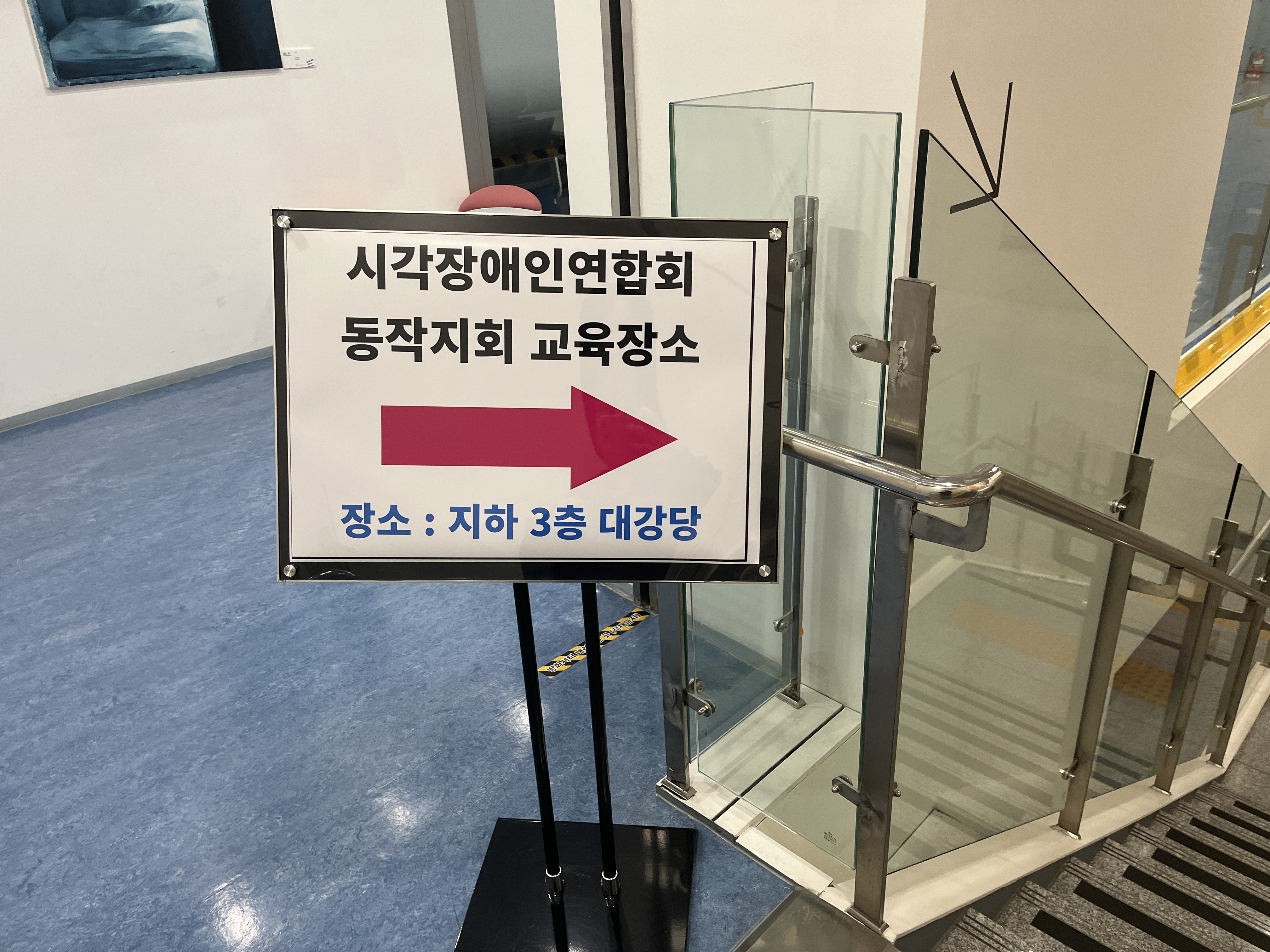 이미지설명: 시각장애인연합회동작지회 교육장소라고 써진 입간판. 교육장소인 대강당을 화살표 그림이 가리키고 있다.