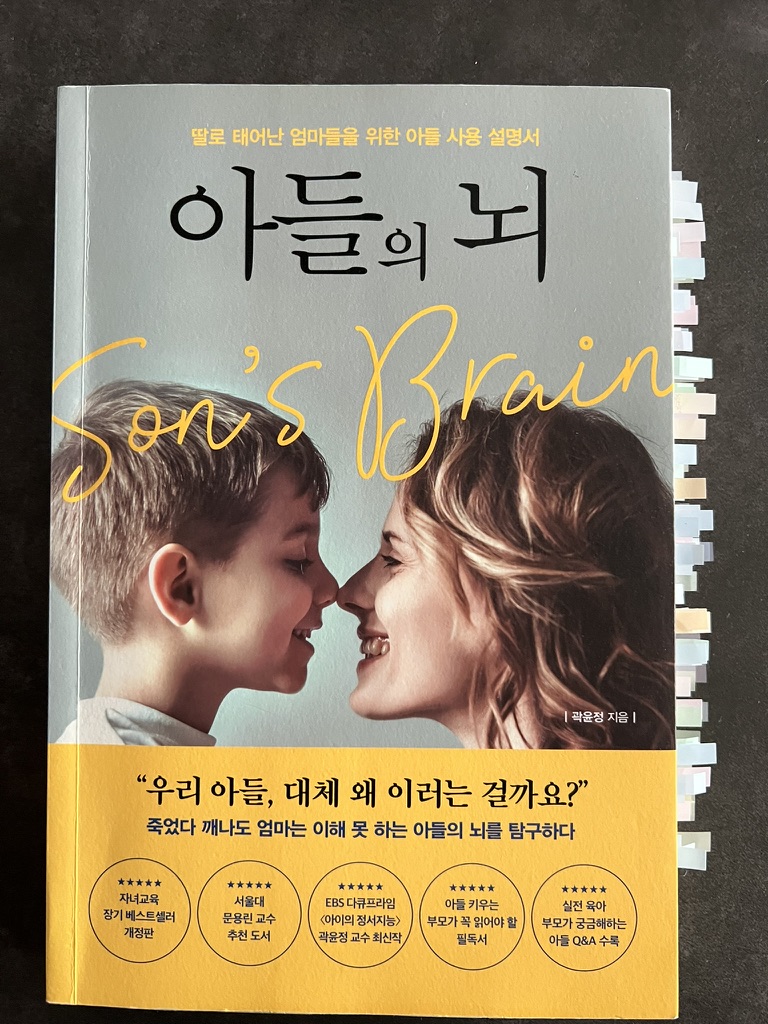 『아들의 뇌』 책 표지. 아이와 엄마가 마주보고 웃는 사진과 함께 “우리 아들, 대체 왜 이러는 걸까요?”라는 문구가 인쇄되어 있으며, 다양한 추천 배지와 인덱스 스티커가 붙어 있다.
