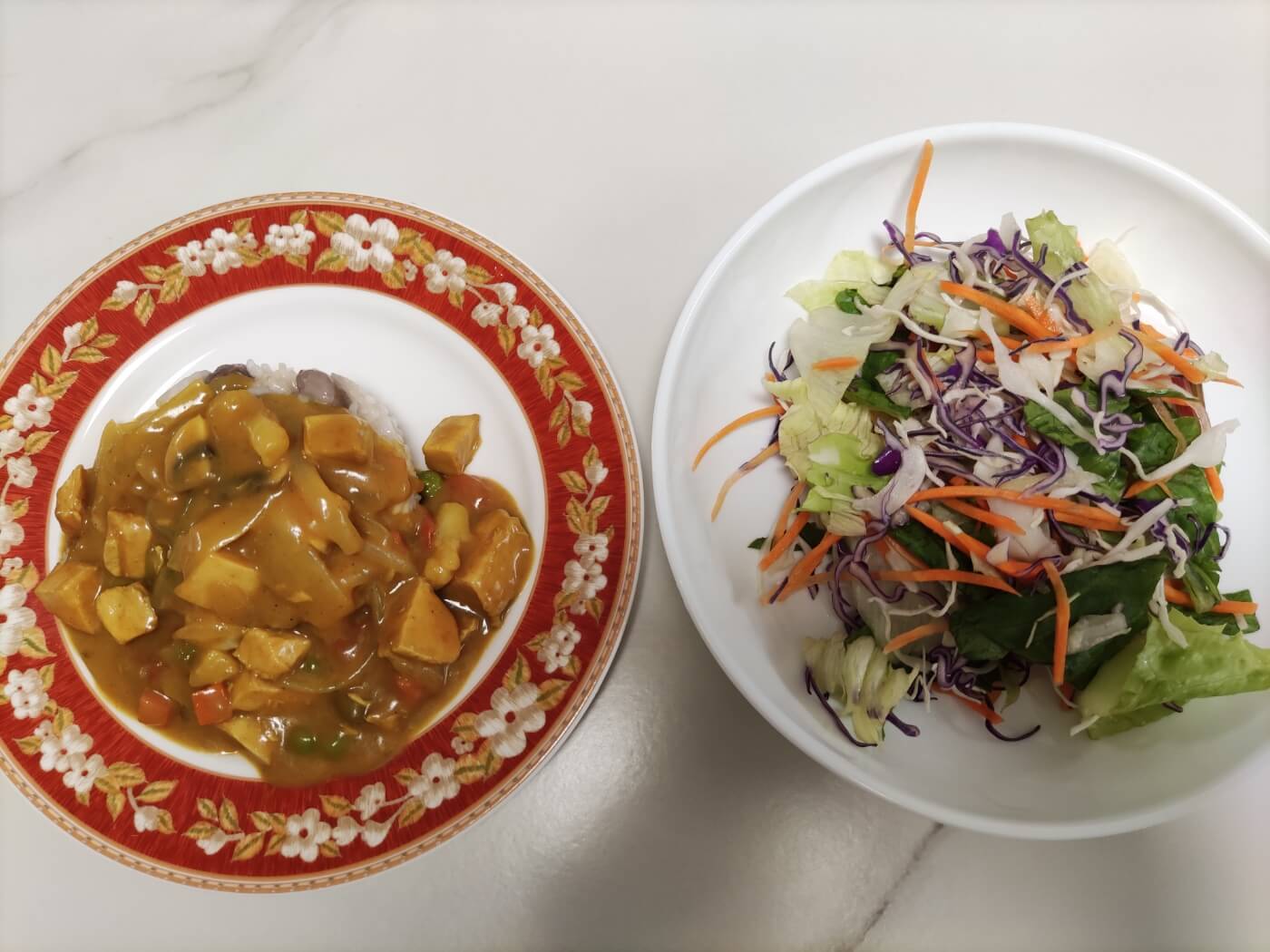 밥이 담긴 카레 접시와 신선한 채소 샐러드 접시가 나란히 놓인 모습