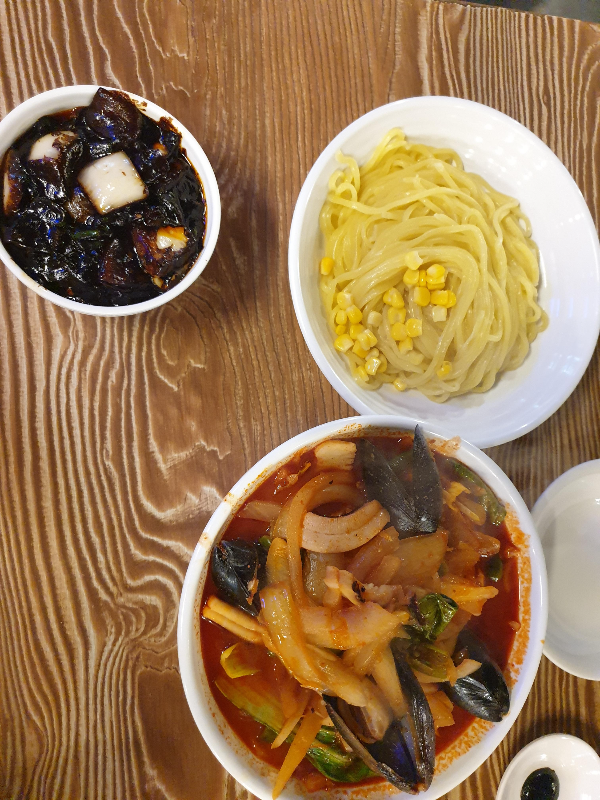 면 위에 옥수수가 올라가 있는 고추 간짜장과 홍합, 오징어가 보이는 고추 짬뽕