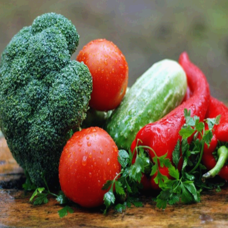 싱싱한 브로콜리, 토마토, 오이, 빨간 파프리카, 파슬리가 나무 테이블 위에 올려져 있습니다. 물방울이 맺힌 채소들은 갓 수확한 듯 신선함이 강조되며, 비타민과 식이섬유가 풍부해 다이어트 식단, 건강식, 면역력 강화에 좋은 재료들입니다. 균형 잡힌 영양을 위한 신선한 채소 섭취의 중요성을 보여주는 장면