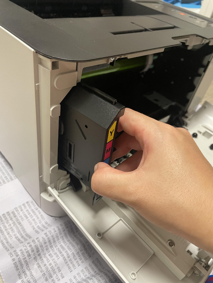 삼성 프린터 폐토너통을 손으로 잡아당겨 빼내는 모습