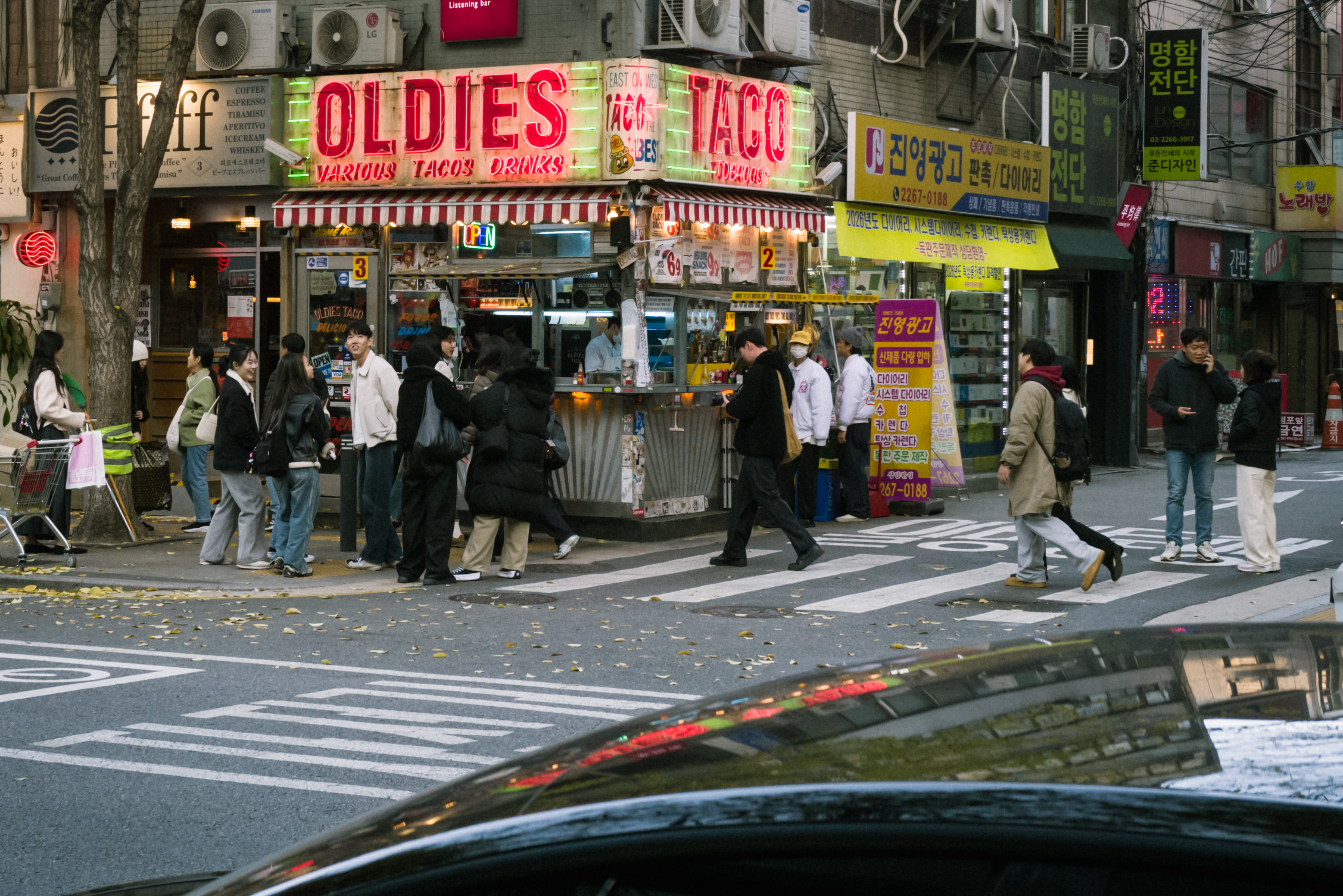 라이카 Q2의 75mm 디지털 줌으로 찍은 사진이다. 네온 사인의 타코 가게 앞에 사람들이 모여있다. 전체적으로 선명한 편이나 중앙부 타코 집 근처에 디테일이 조금 떨어지는 모습을 보인다.