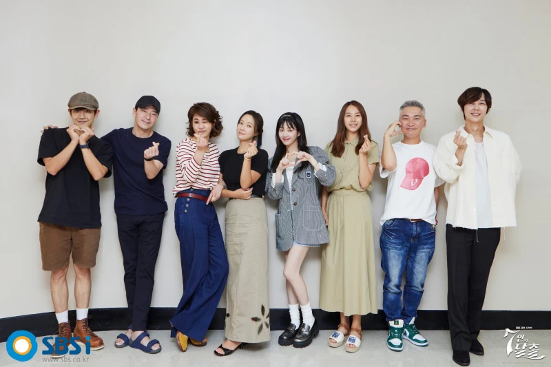 어느 흰벽을 등뒤로 7인의 탈출에 출연하는 주연 배우들이 손가락 하트를 하면서 단체 사진을 찍고 있는 이미지