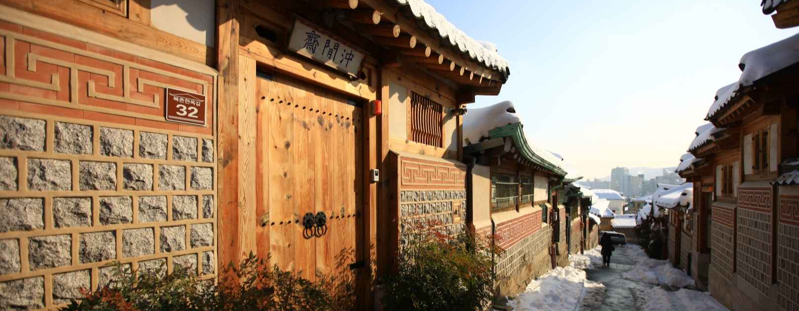 북촌 한옥마을 골목- 기와 지붕 위에 눈이 쌓여 있고 대문과 장식이 된 담벼락의 모습.