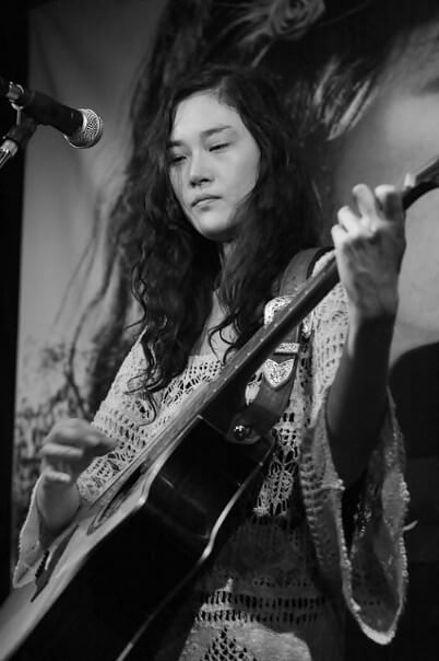 손지연이-스탠드-마이크-앞에-서서-기타를-치는-흑백-사진