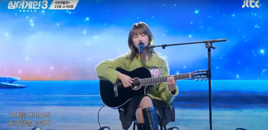 싱어게인 3- 파란색을 배경으로 가슴에 60번호표를 달고 연두색 상의를 입고 단발머리를 늘어뜨린채 기타를 치며 노래하는 60호 전신이미지