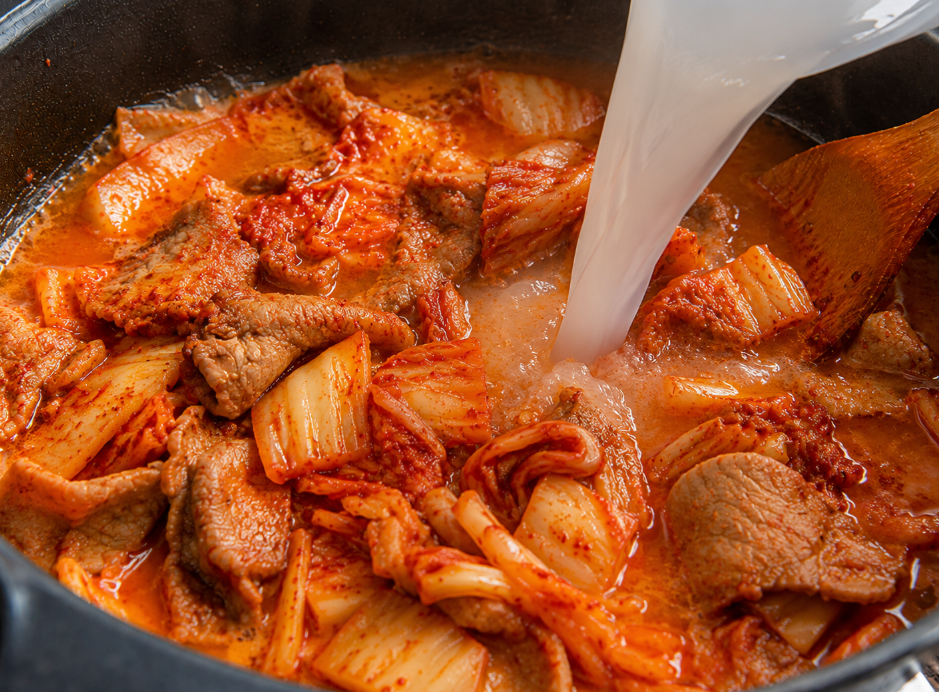 볶아진 김치 위로 뽀얀 쌀뜨물이 부어지며 국물이 풍성해지는 모습.