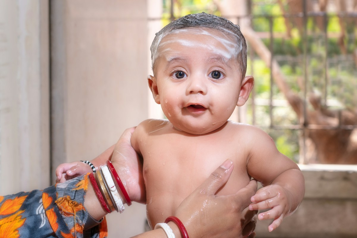 Cute baby with soap on head being bathed