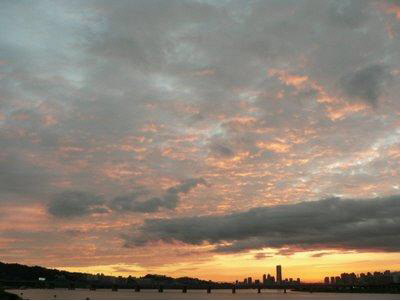 반포대교 위에서 여의도와 용산, 마포 방향을 바라본 일몰 무렵의 전경. 붉게 물든 구름이 하늘에 흩어져 있으며, 전경에는 한강대교와 그 뒤로 우뚝 솟은 63빌딩이 뚜렷하게 보인다. 한강 너머로는 도시의 실루엣이 어슴푸레 펼쳐진다.