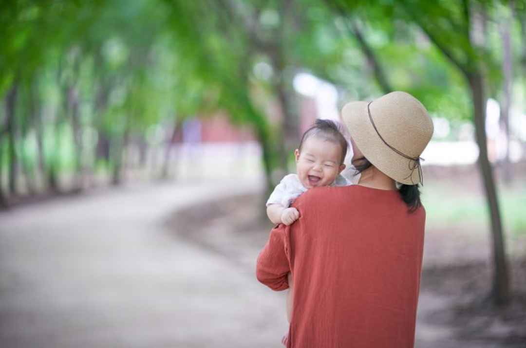 한 엄마가 아기를 안고 있고 아기는 환하게 웃고 있다.