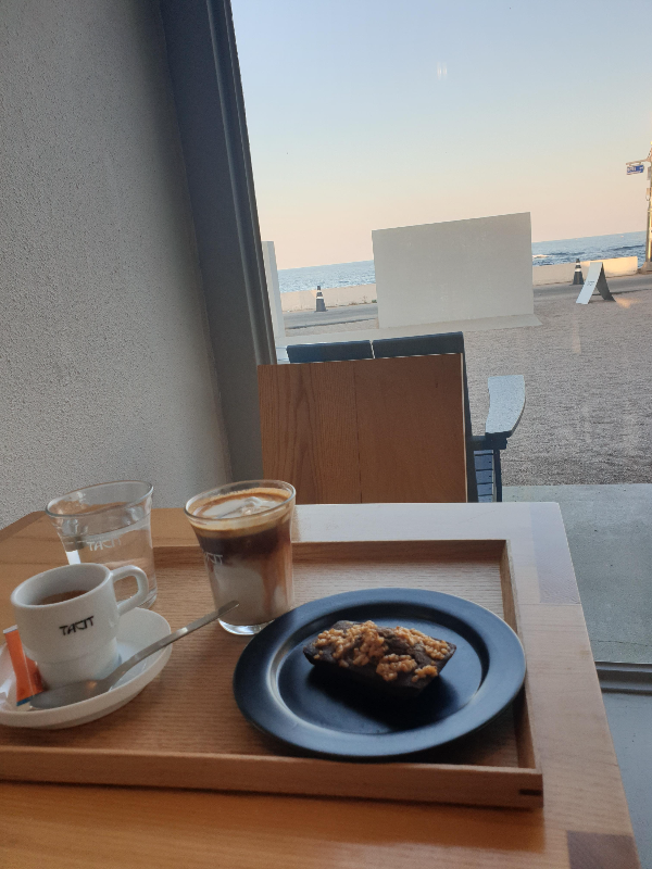 창문 너머 바다가 보이고 테이블 위에는 주문한 음료가 놓여있다.