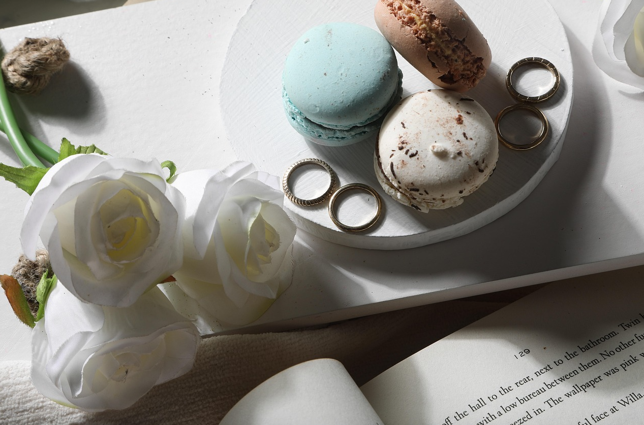 책상위에 책이 펼쳐져 있고 꽃과 마카롱이 놓여 있다