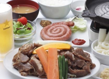 흰 접시 위에 고기가 올라가 있고 주위로 맥주 등 다른 반찬들이 보인다